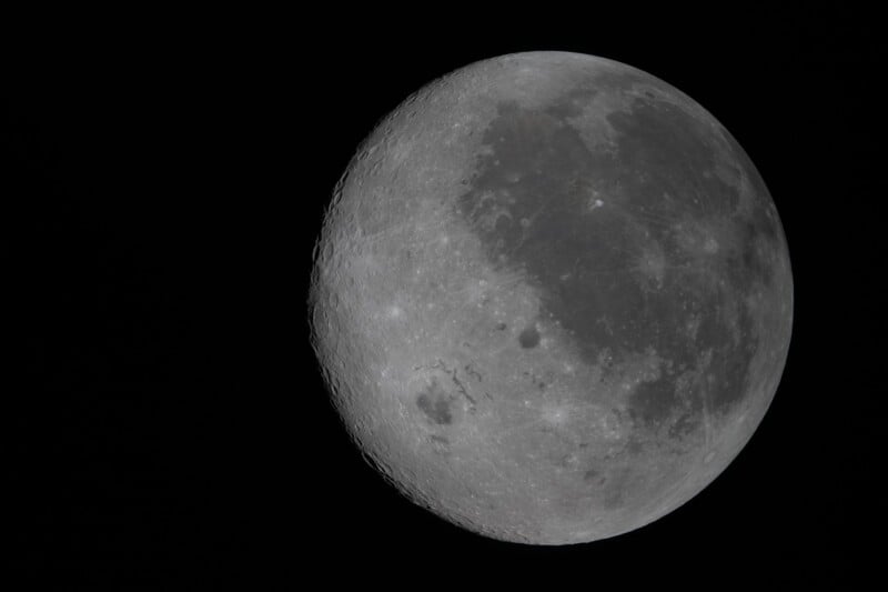 A detailed close-up image of the moon against a black sky, showing its craters and surface textures with one side slightly shadowed.