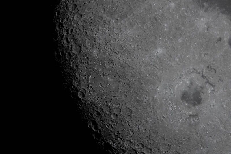 Close-up image of the Moon’s surface, showing numerous craters and rugged terrain in sharp detail, with the left side fading into darkness.