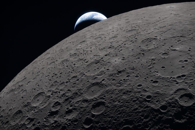 View of the Moon’s cratered surface in the foreground with planet Earth partially visible rising over the lunar horizon against the blackness of space.