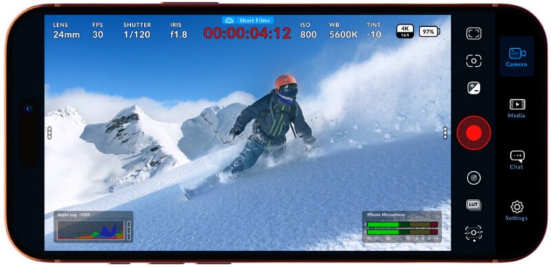 A smartphone screen displays a camera app interface recording a snowboarder riding down a snowy mountain slope, surrounded by snow-covered peaks under a clear blue sky. Camera settings and controls appear on the screen.