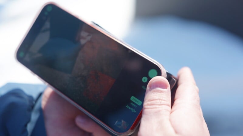 A person holds a smartphone in both hands, with a messaging app open on the screen. The background is blurred, and the phone displays a message conversation.