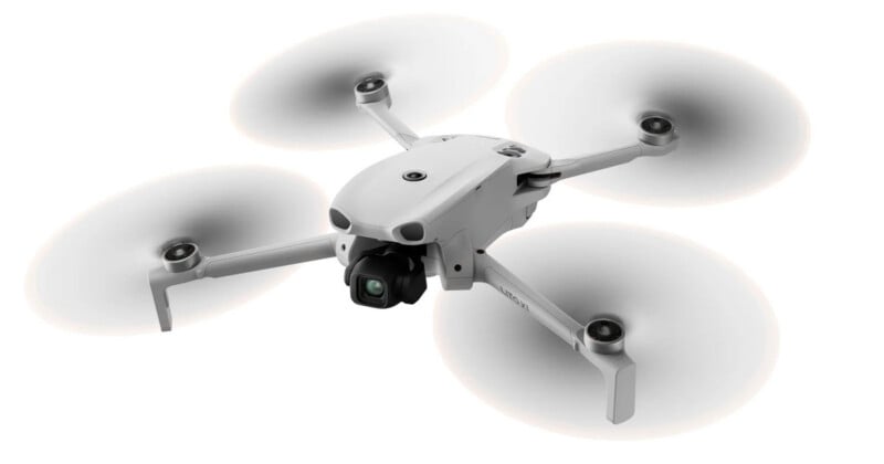 A white quadcopter drone with four spinning propellers and a camera mounted on its front, isolated on a white background.