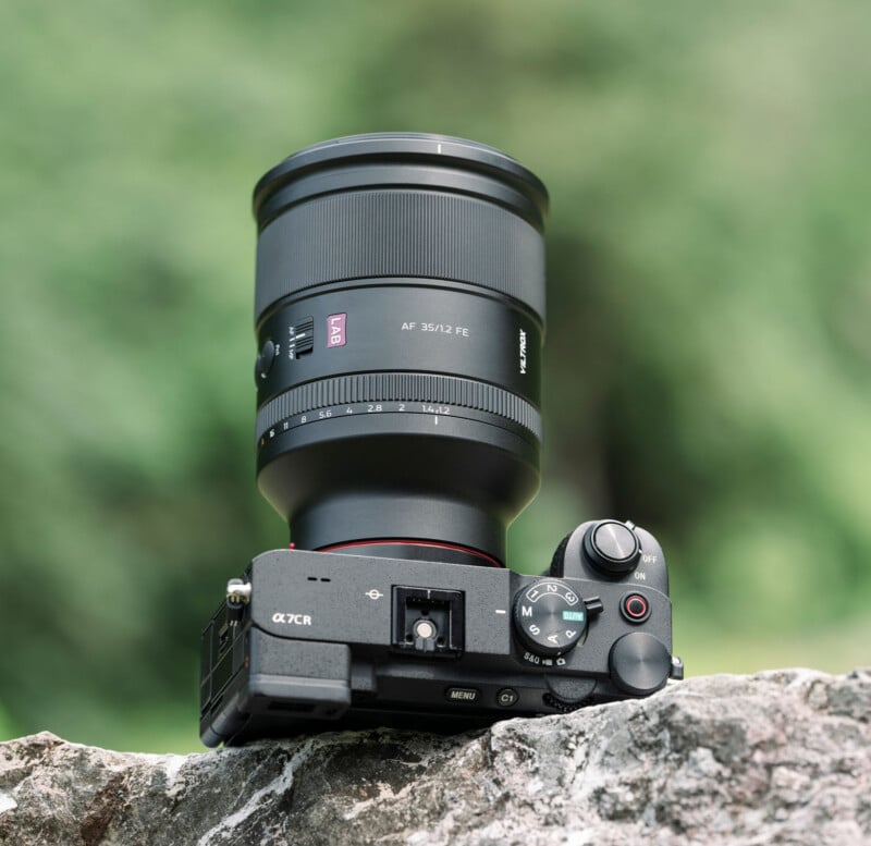 A black Sony Alpha 7CR camera with a large AF 35mm f/1.2 FE lens rests on a rough stone surface, with a blurred green background.