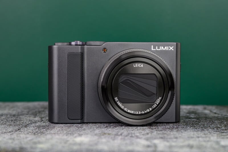 A black Panasonic Lumix digital camera with a Leica lens sits on a textured gray surface against a green background.