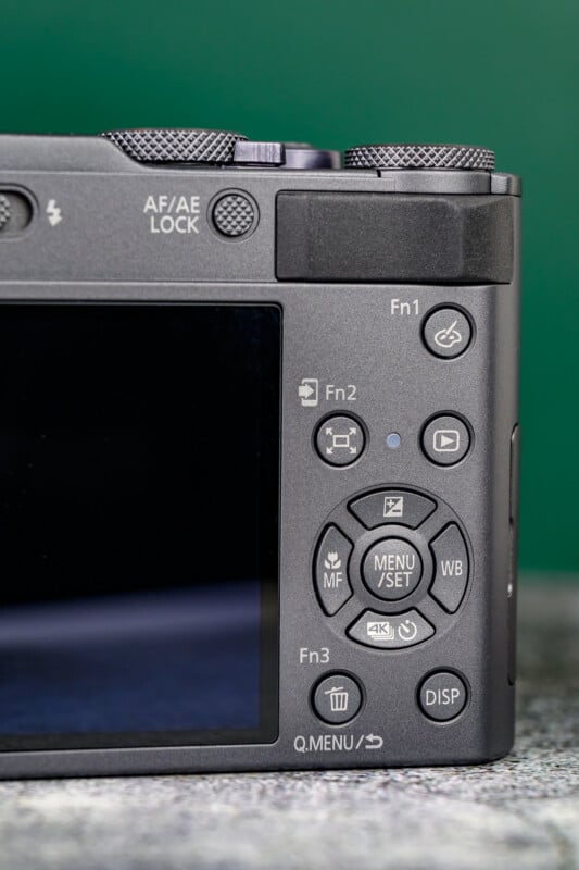 Close-up of the back of a digital camera showing control buttons, including Fn1, Fn2, Fn3, a directional pad, MENU/SET button, DISP button, and part of the LCD screen on a green background.