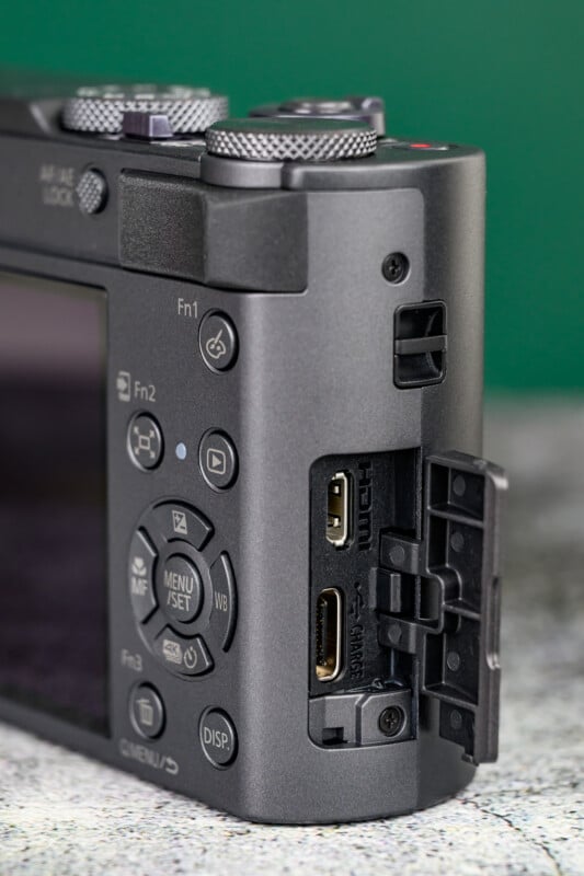 A close-up view of the side of a digital camera shows an open port cover revealing HDMI and USB-C ports, with various control buttons visible on the camera body.
