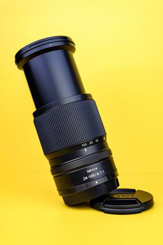A Nikon NIKKOR 24-105mm f/4-7.1 camera lens stands upright on a matching lens cap against a bright yellow background.