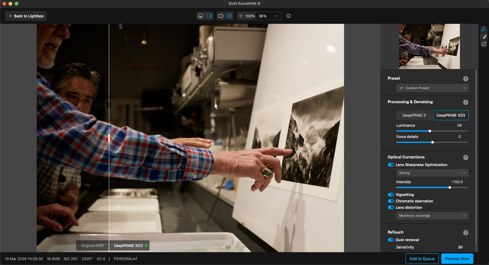 A person points at a black-and-white mountain photograph on a table in a workspace, while another observes; editing software interface with image adjustments is visible on the right side of the screen.