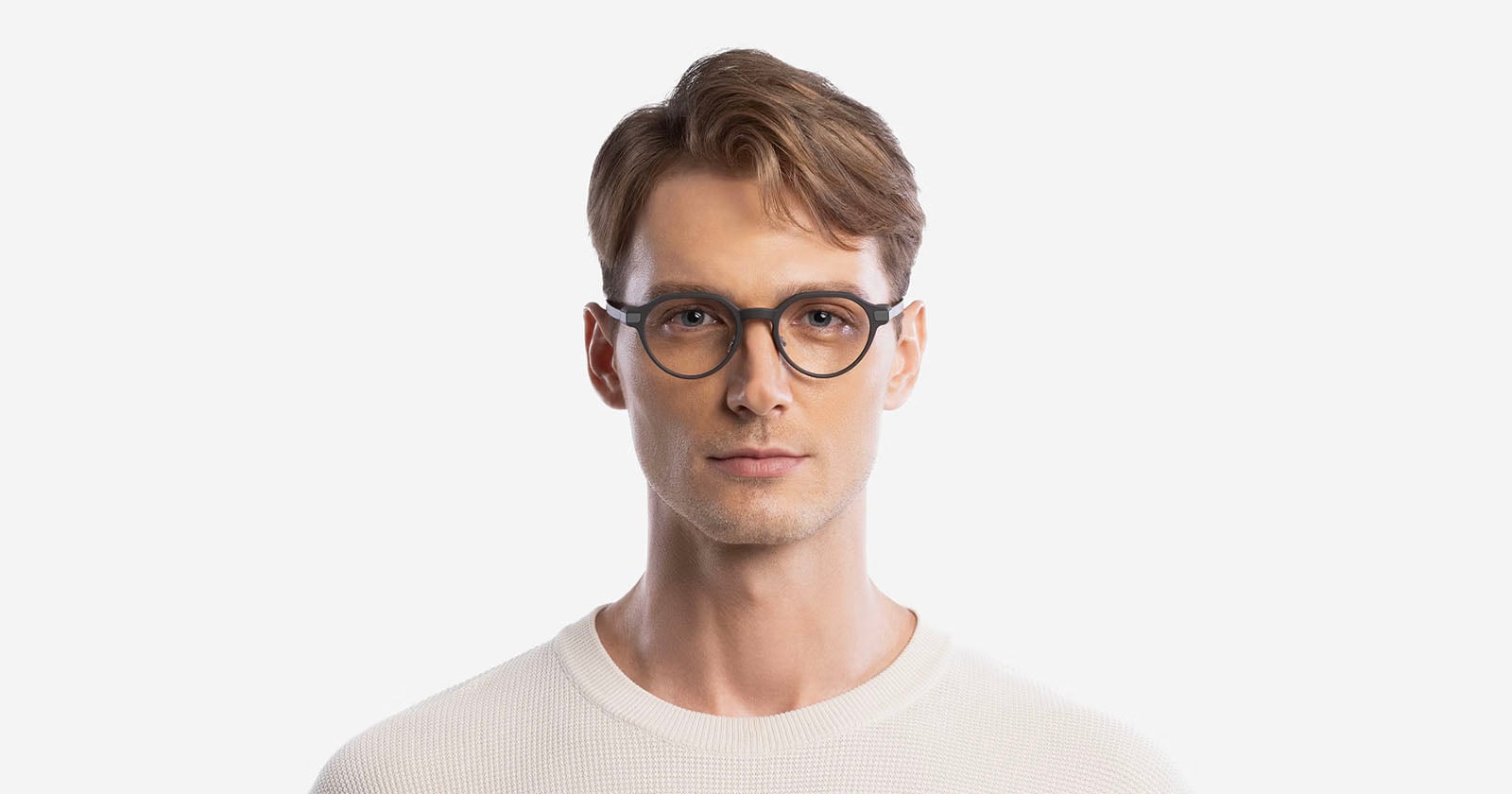 A young man with light brown hair wearing round black eyeglasses and a white textured sweater, standing against a plain white background.
