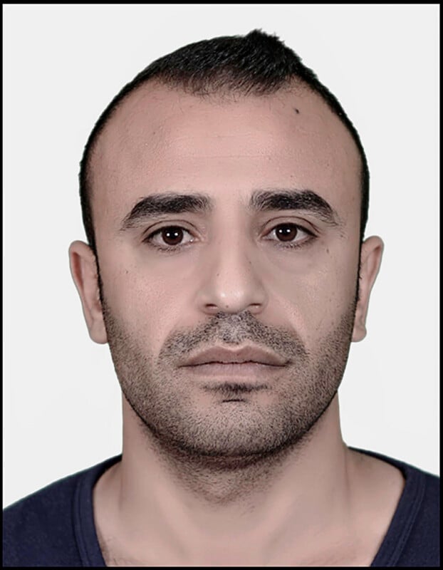 A man with short, dark hair and a trimmed beard looks directly at the camera with a neutral expression, set against a plain light background.