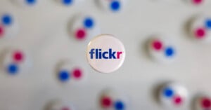 A round pin with the Flickr logo in blue and pink text is centered in focus, with several blurred pins featuring the same colors in the background.