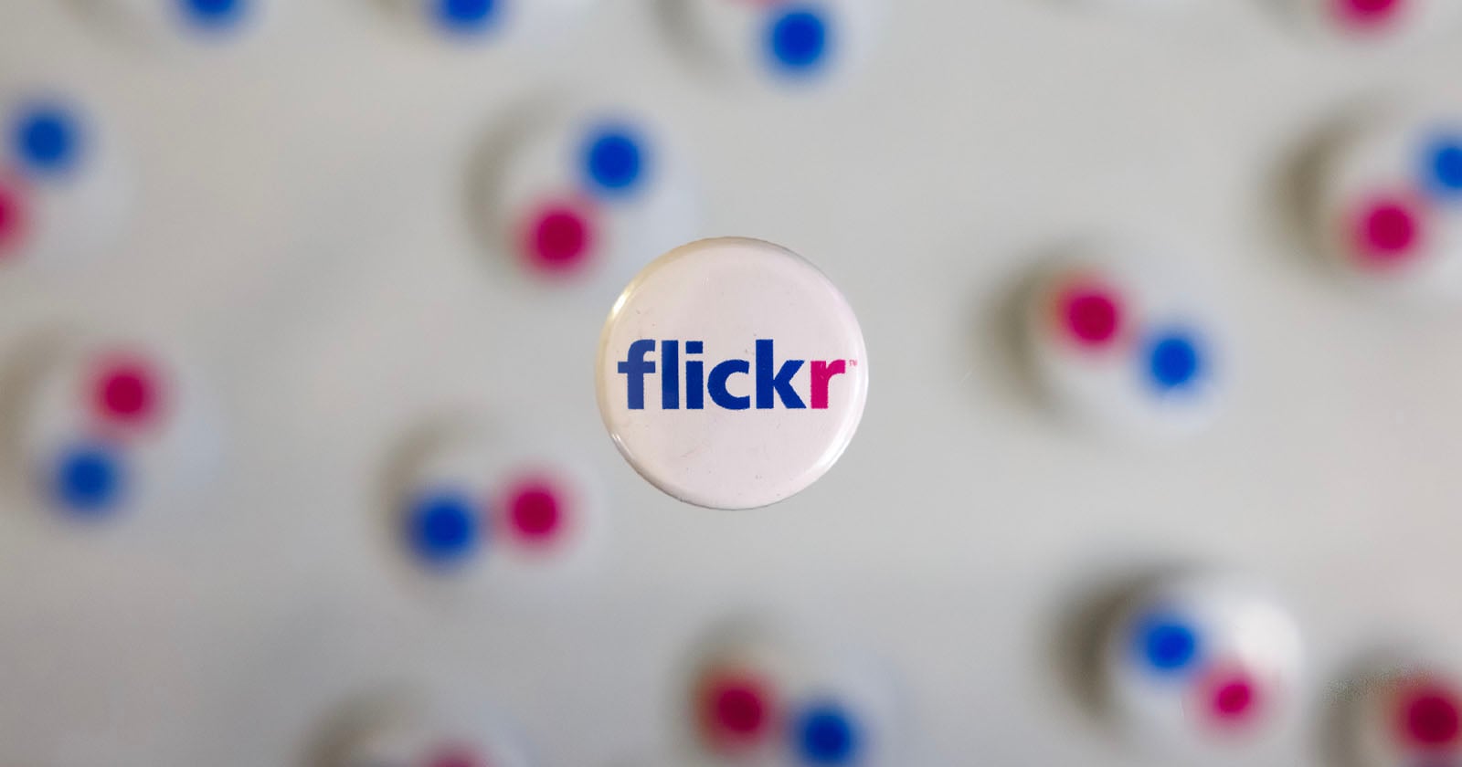 A round pin with the Flickr logo in blue and pink text is centered in focus, with several blurred pins featuring the same colors in the background.