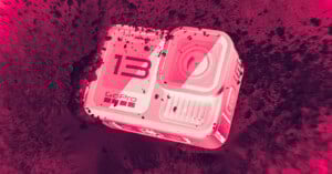 A GoPro HERO13 action camera partially covered in dirt, lying at an angle on a rough surface. The image has a bold pink and red color filter, giving it a dramatic, high-contrast appearance.