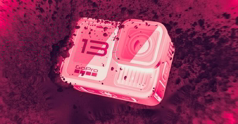 A GoPro HERO13 action camera partially covered in dirt, lying at an angle on a rough surface. The image has a bold pink and red color filter, giving it a dramatic, high-contrast appearance.