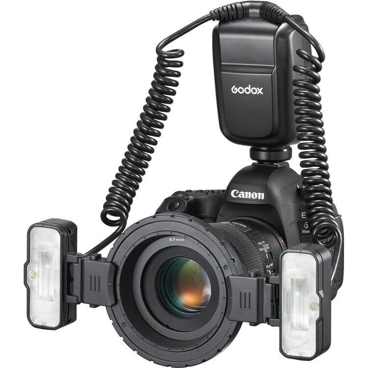 A Canon camera equipped with a Godox flash unit and a macro ring flash attachment mounted on the lens, with coiled cables connecting the flash to the controller.