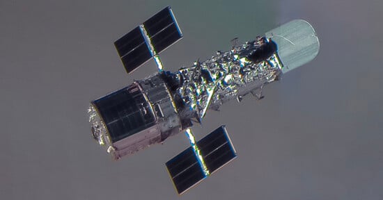 A close-up view of a space telescope with solar panels extended on either side, floating against the backdrop of space with a faintly visible planet or atmosphere.