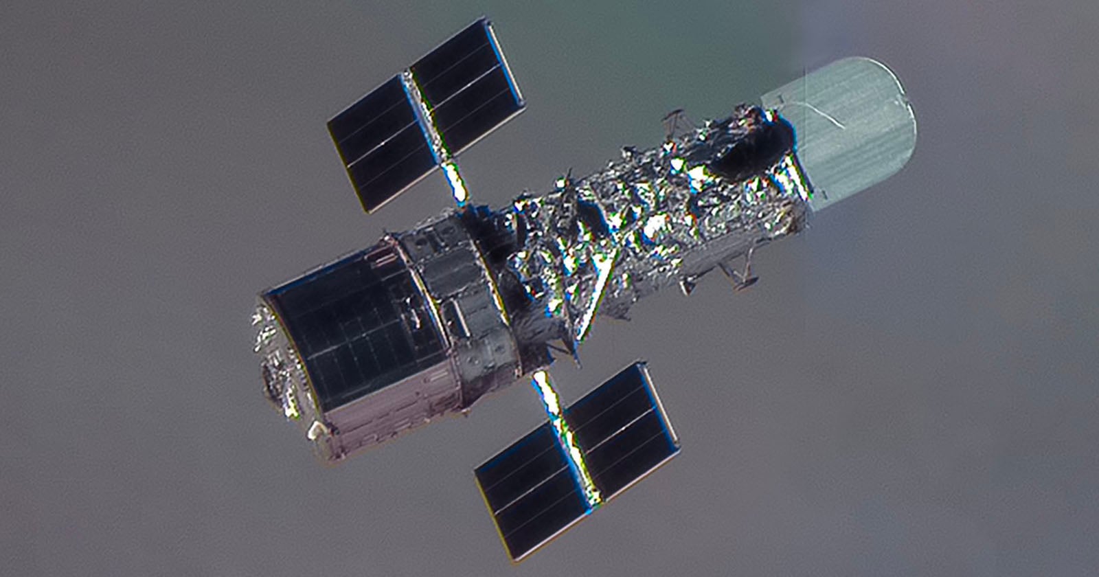 A close-up view of a space telescope with solar panels extended on either side, floating against the backdrop of space with a faintly visible planet or atmosphere.