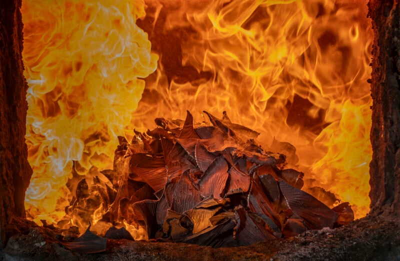 A pile of shark fins burns intensely inside a furnace, surrounded by bright orange and yellow flames.