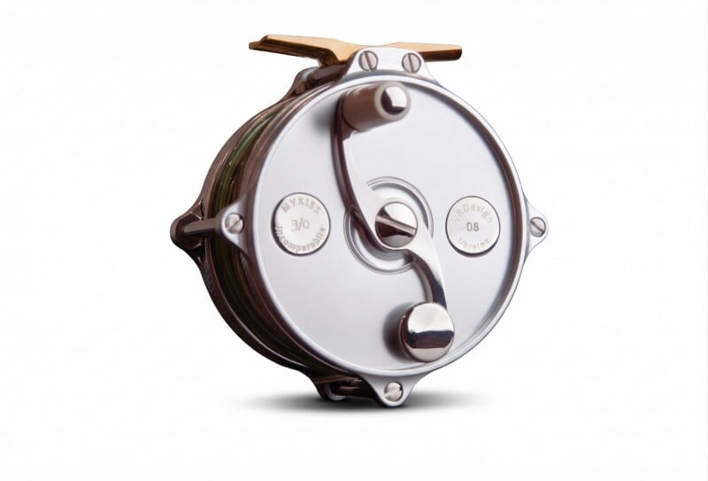 A close-up of a metallic fishing reel with a smooth, shiny surface and engraved markings, isolated on a white background.