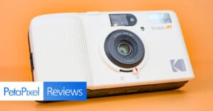 A white Kodak Snapic AI camera with a 25mm Kodak lens is displayed on an orange background. At the bottom left, a PetaPixel Reviews logo is visible.