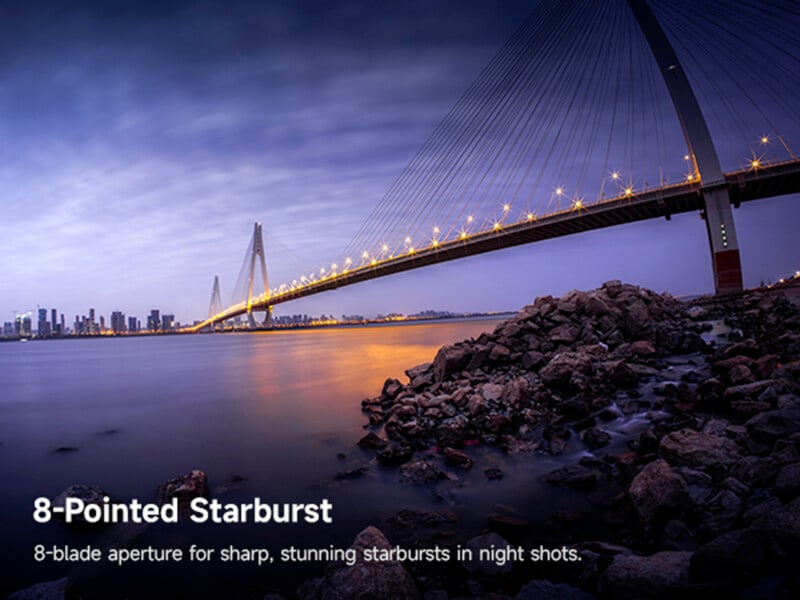 Un paisaje urbano nocturno muestra un puente atirantado iluminado con un efecto de explosión de luces que abarca un río tranquilo con rocas en primer plano y el horizonte en la distancia. El texto es el siguiente: "Estallido estelar de las 8 en punto.