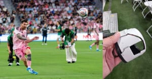 Lionel Messi kicks a soccer ball during a match, with photographers in the background. On the right, a hand holds a broken pitch-side camera, showing significant damage.