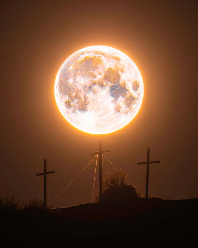 Una brillante luna llena brilla en el cielo nocturno directamente sobre tres cruces recortadas en la montaña, creando una espectacular escena brillante donde la luna aparece como un halo.