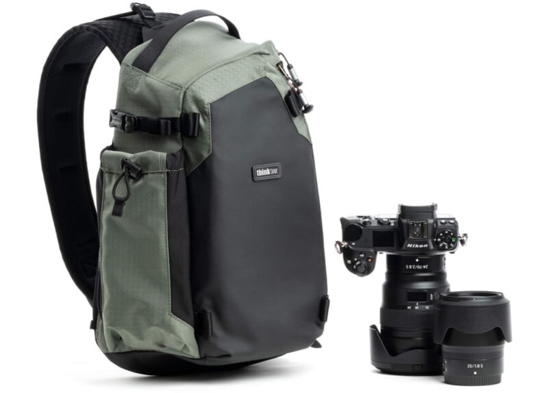 A green and black camera backpack sits next to a digital camera with a lens attached and an additional lens placed on a white surface.