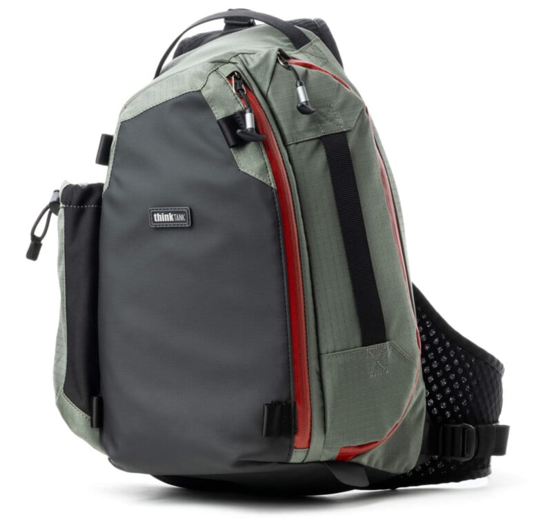 A gray and green sling backpack with a black mesh padded strap, red accents, zippered pockets, and a "thinkTANK" logo on the front.
