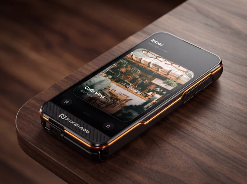 A modern smartphone with a rugged case rests on a wooden surface, displaying an email inbox with a photo of a cafe interior on its screen. The case features orange accents and the brand name "PIXELmob.