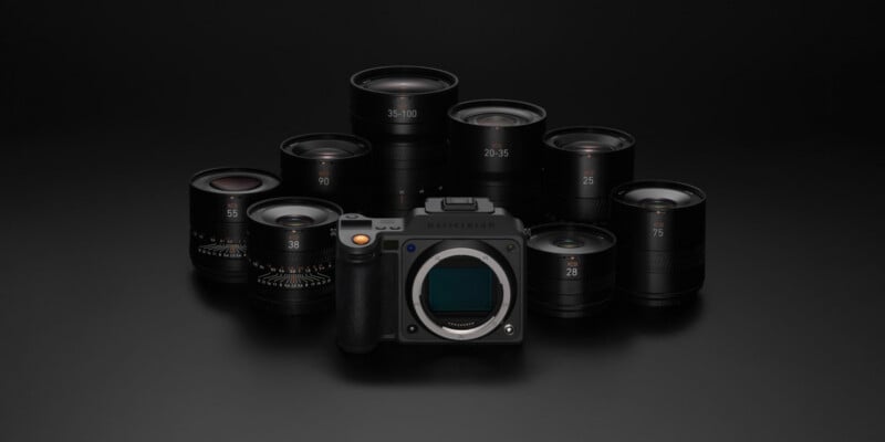 A professional camera body is displayed on a dark surface, surrounded by eight interchangeable camera lenses arranged in a semicircle behind it. The scene is softly lit, highlighting the camera equipment.