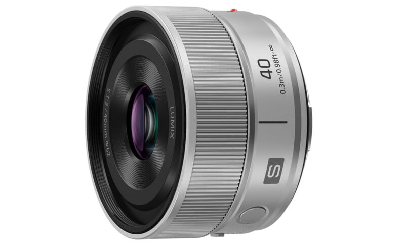 A silver Panasonic Lumix S 40mm f/1.8 camera lens is shown angled to display its glass element, focus ring, and engraved markings, including the focal length, aperture, and minimum focusing distance.
