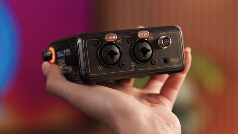 A hand holds an audio interface showing two combo XLR/TRS input ports, a power input, and additional connectors, with a blurred colorful background.