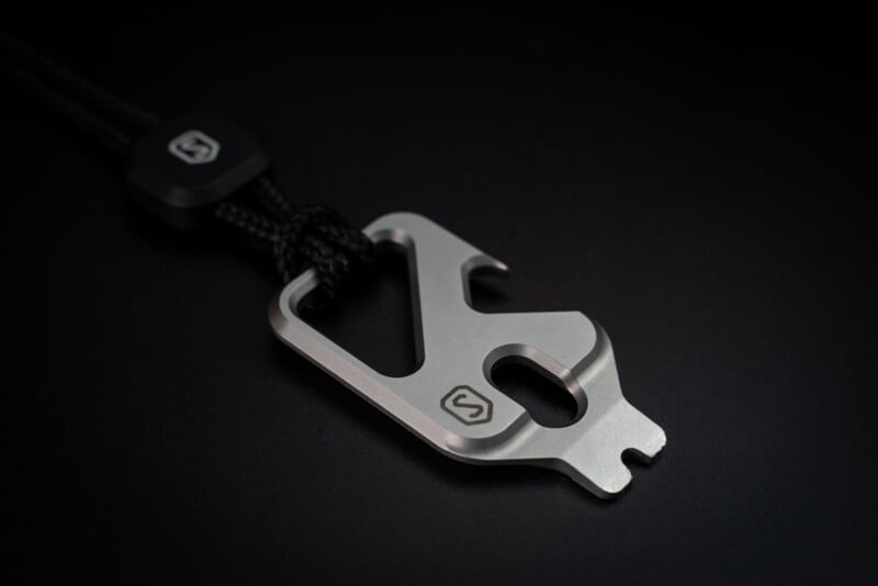 A close-up of a metallic multitool with a black cord attached, featuring a sleek design and engraved logo, placed on a dark surface.