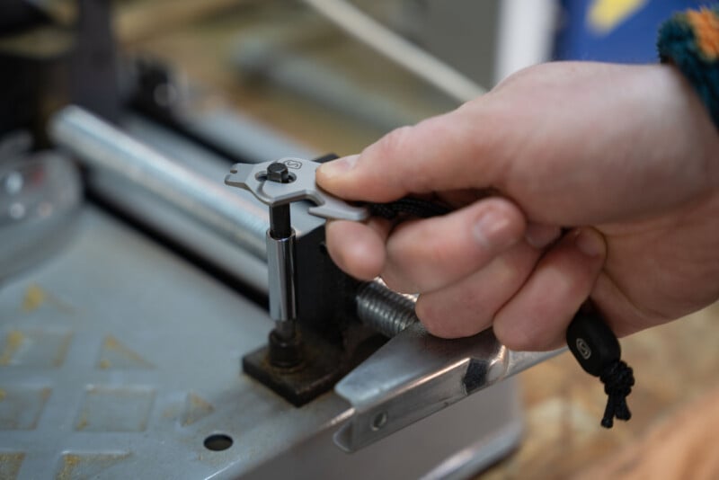 A close-up of a hand using a small multi-tool to adjust or tighten a bolt on a metal machine in a workshop setting.