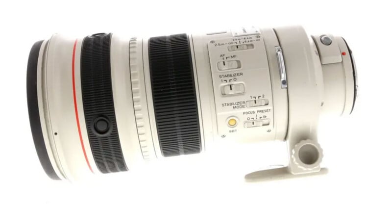 A white professional telephoto camera lens with black and red accents, multiple control switches, and a tripod mount, photographed against a white background.