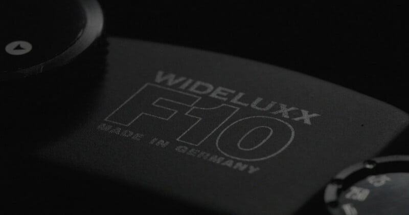 Close-up of the engraved text "WIDELUXX F10 MADE IN GERMANY" on a dark camera body with part of a dial and button visible in low lighting.
