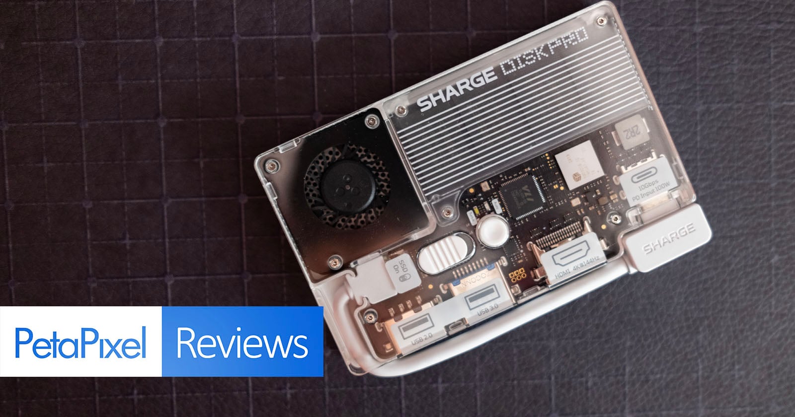 A transparent electronic device with visible internal components labeled "SHARGE" rests on a dark textured surface. The image features the "PetaPixel Reviews" logo in the bottom left corner.