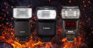 Three camera flashes—Sony, Canon, and Nikon—are displayed upright side by side against a dark background with dramatic orange flames rising beneath and behind them.