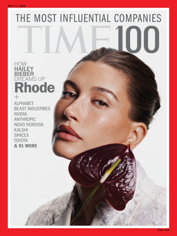 A TIME magazine cover featuring Hailey Bieber with slicked-back hair, holding a dark purple anthurium flower near her chin. The text highlights "The Most Influential Companies" and mentions her brand, Rhode.