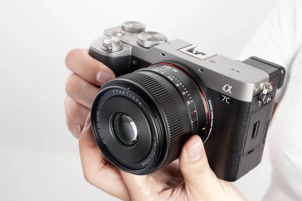 A person holds a Sony Alpha 7C digital camera with a TTArtisan 35mm f/1.4 lens, showcasing the camera body and lens details against a plain white background.
