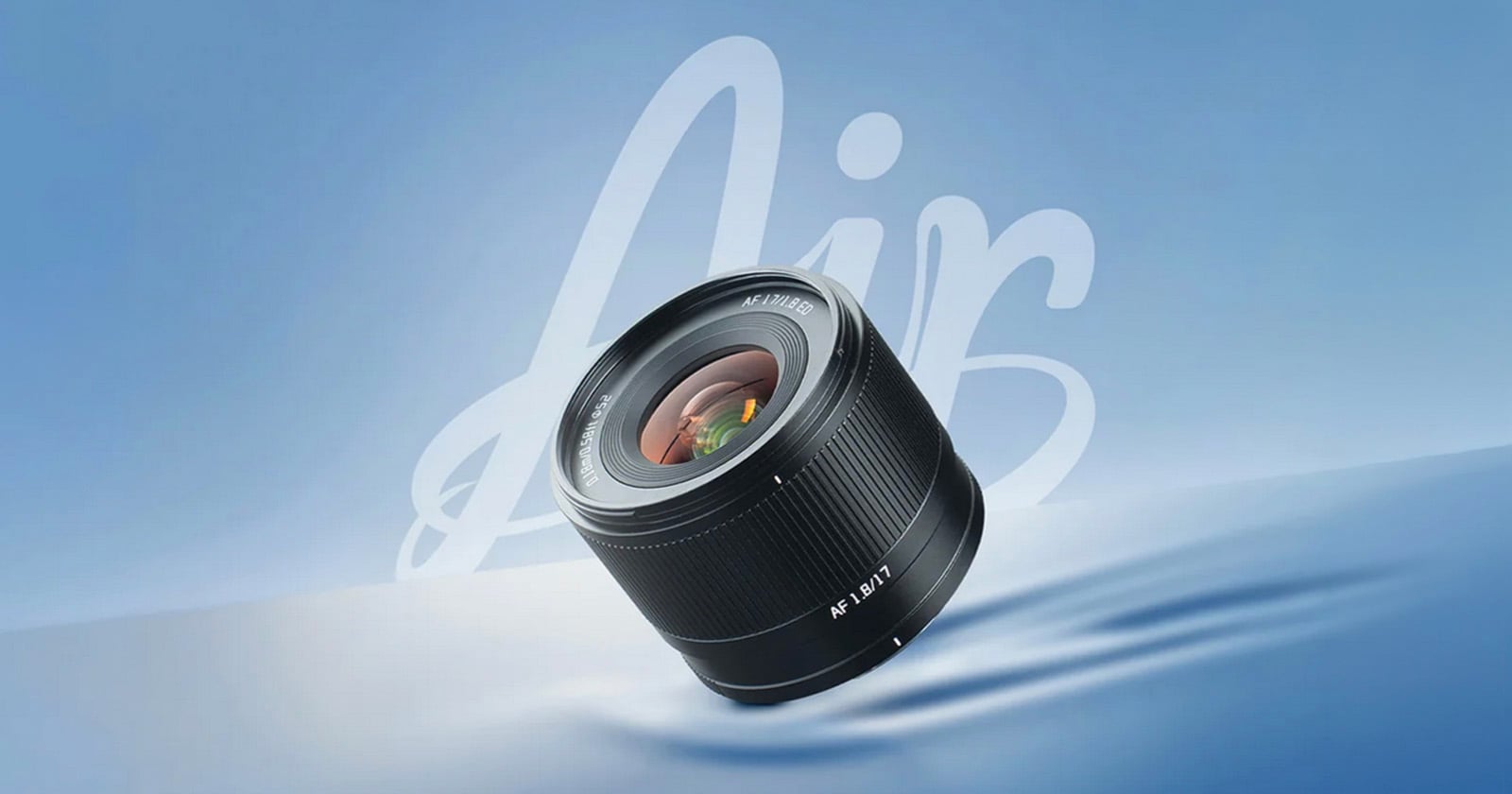 A camera lens labeled "AIR 12mm F2" is displayed against a smooth blue background with the word "Air" written in large, white script behind it. The lens reflects light and appears to be floating.