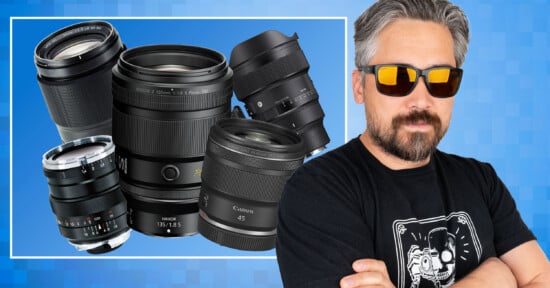 A man with gray hair and a beard, wearing sunglasses and a black t-shirt, stands with arms crossed. Behind him is an illustration of several camera lenses on a blue, pixelated background.