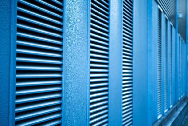 Close-up of blue metal louvered panels lined up on a building exterior, creating a repetitive geometric pattern with angled slats and shadows.