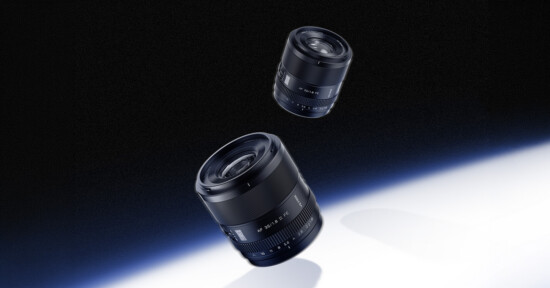 Two camera lenses, one larger and one smaller, are floating above a white and blue gradient surface with a black background, giving the appearance of them hovering in space.