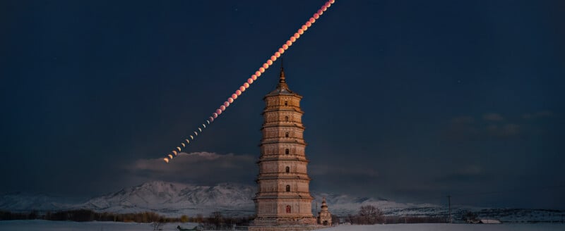 A tall, ancient pagoda stands in front of snow-covered mountains at night, with a sequence of red and white moon phases arcing across the dark sky above it.