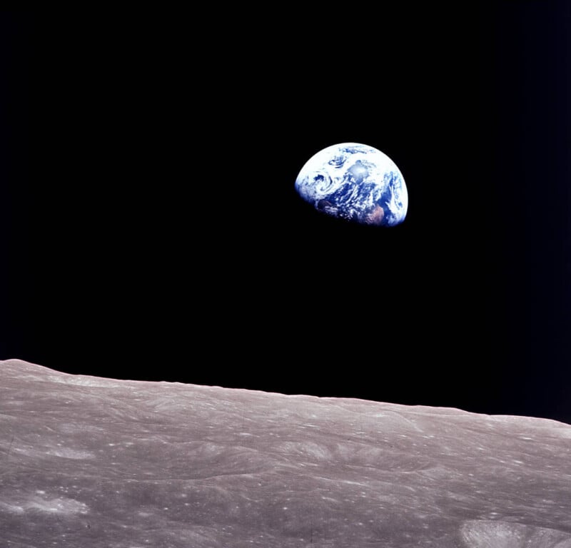 View of Earth rising over the barren, gray surface of the Moon, set against the blackness of space. The Earth appears partly illuminated, with visible continents and clouds.