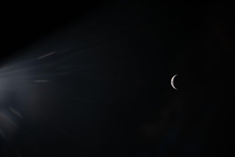 A crescent moon appears on the right side of a dark sky, with bright light rays streaming in from the left, creating a dramatic contrast between light and shadow.