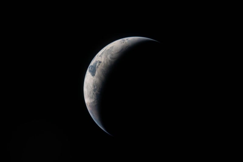 A crescent-shaped view of Earth in space, with part of the planet illuminated and the rest in shadow, set against a completely black background.