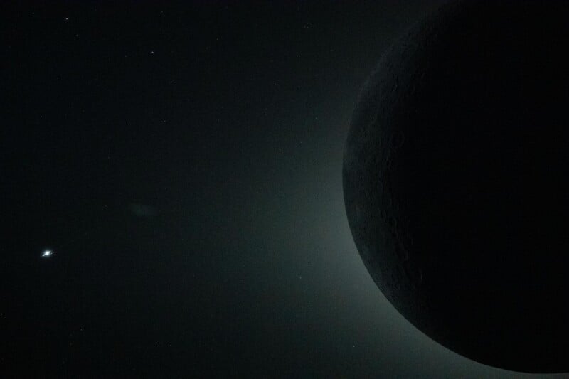 A dark, partially visible moon appears against a black sky with faint stars scattered in the background and a bright celestial object on the left.